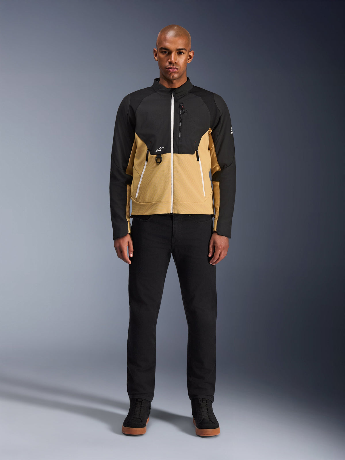 Veste Alpinestars Provoke en Noir Camel, veste de moto urbaine au design bicolore noir et camel, portée par un mannequin avec un pantalon noir et des chaussures noires, silhouette contemporaine avec fermetures éclair blanches et construction technique en softshell.