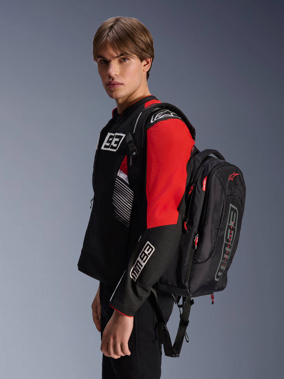Sac à dos Alpinestars MM93 City Hunter V2, noir avec accents rouges, porté par un mannequin avec une veste de moto MM93 assortie noire et rouge, logos et marquages Marc Márquez, équipement de conduite urbaine
