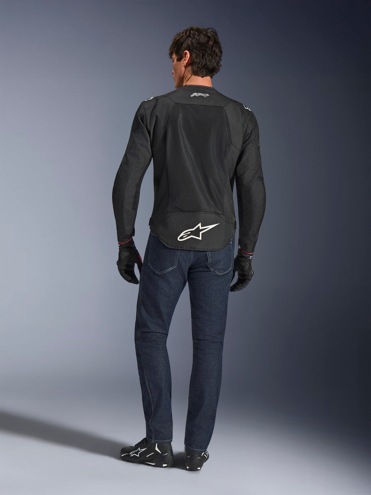 Alpinestars FQ20 T-SPS Air V2 Monster Jacket, Black, rear view on model wearing dark blue jeans and black riding boots, featuring a large white logo on the lower back and breathable mesh panels, urban sport riding gear