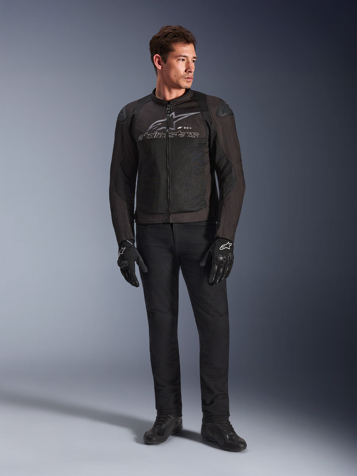 Mannequin homme portant la veste de moto Alpinestars SMX Air, coloris Black Anthracite, avec panneaux en maille ventilée et logo gris sur la poitrine, associée à un pantalon noir et des gants de protection, studio avec fond en dégradé