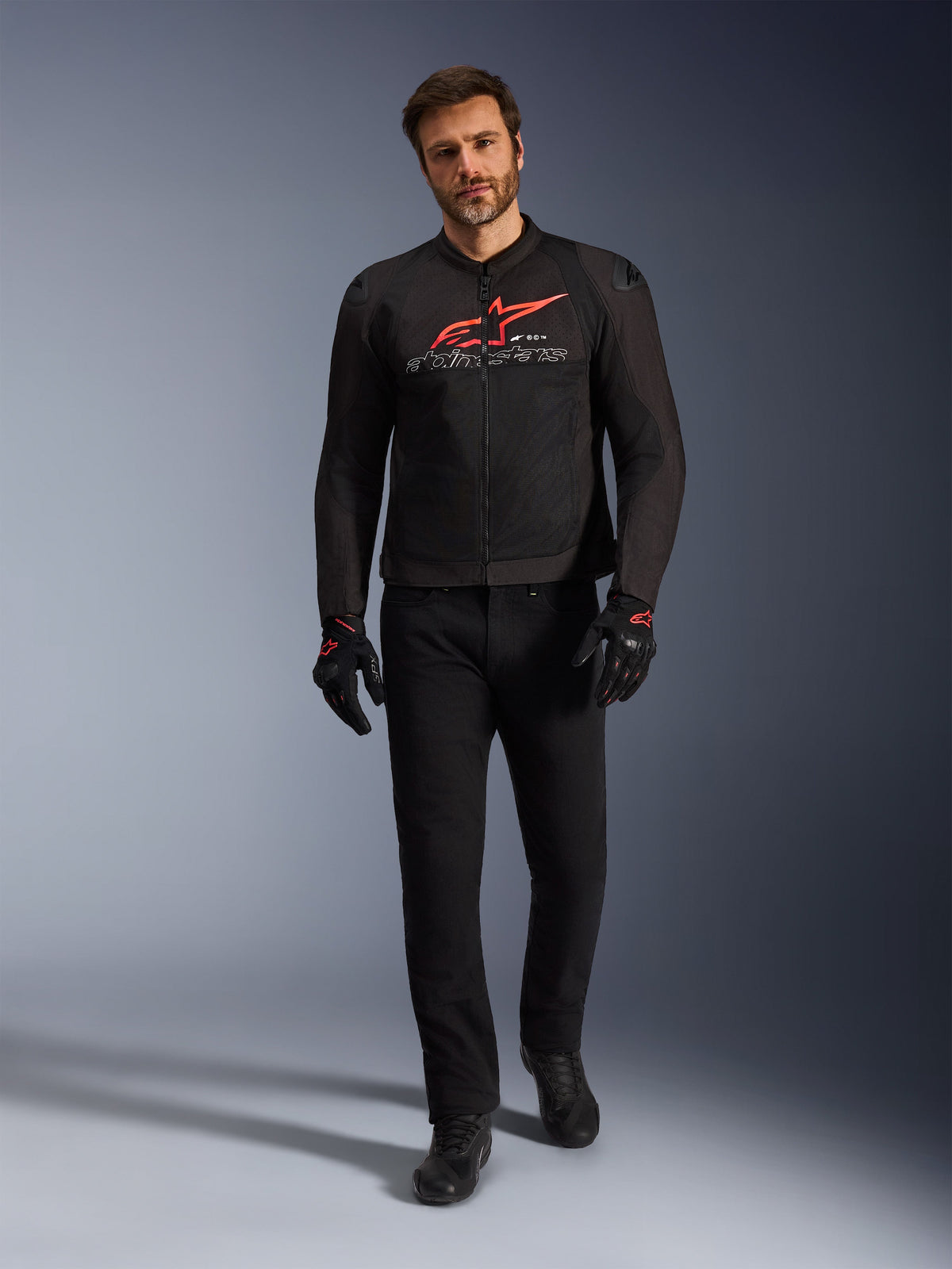 Veste Alpinestars SMX Air, noir, rouge vif et blanc, veste de moto sportive portée avec un pantalon et des gants de moto noirs, dotée de panneaux en maille technique et d'un logo Alpinestars rouge vif sur la poitrine, tenue de route haute performance