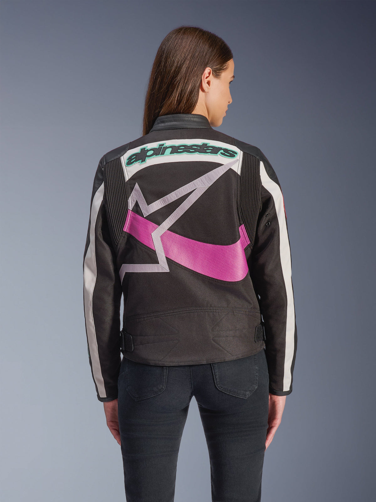 Veste Alpinestars Idles pour femme, vue de dos, noir, blanc cassé et violet, grand logo étoile graphique au dos, mot-symbole brodé bleu sarcelle, panneaux en accordéon sur les épaules, équipement de moto urbain d'inspiration vintage