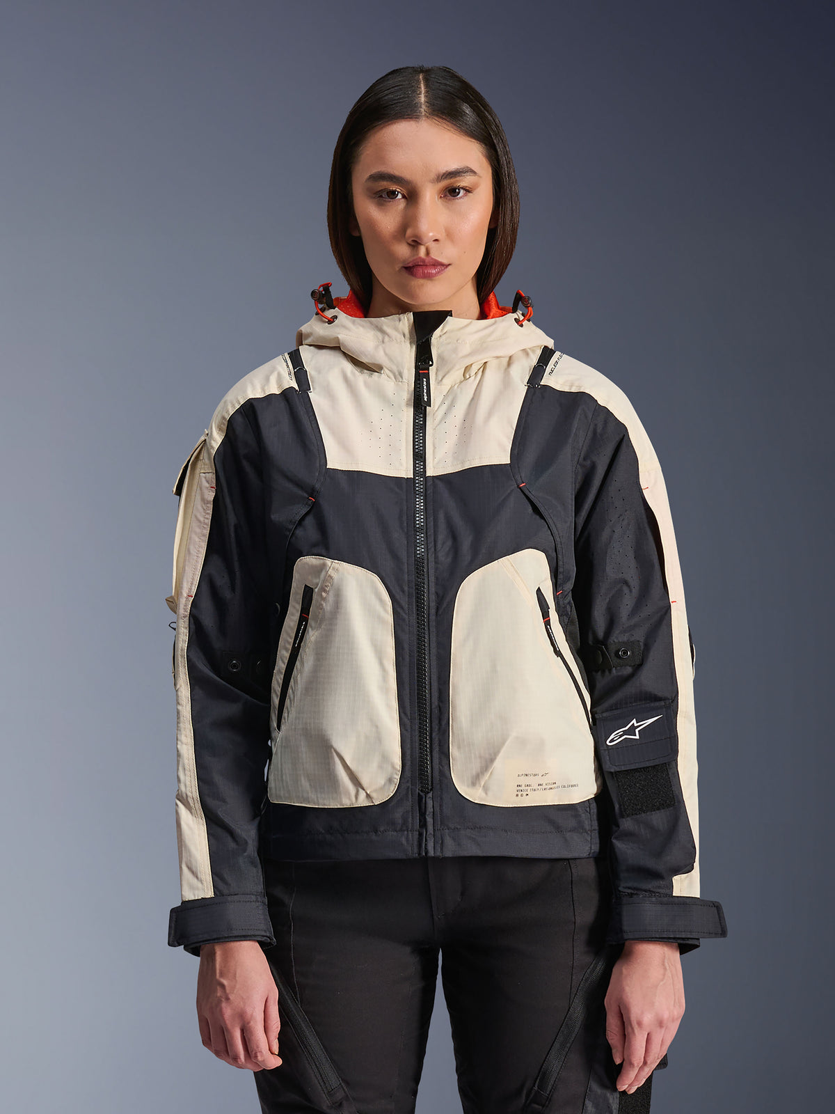 Veste Alpinestars Molly Air, veste de moto urbaine pour femme, Black Almond, vue de face sur un modèle, avec empiècements ripstop crème et noirs, capuche avec doublure orange, fermeture éclair centrale et grandes poches utilitaires, équipement de moto d'inspiration streetwear contemporaine