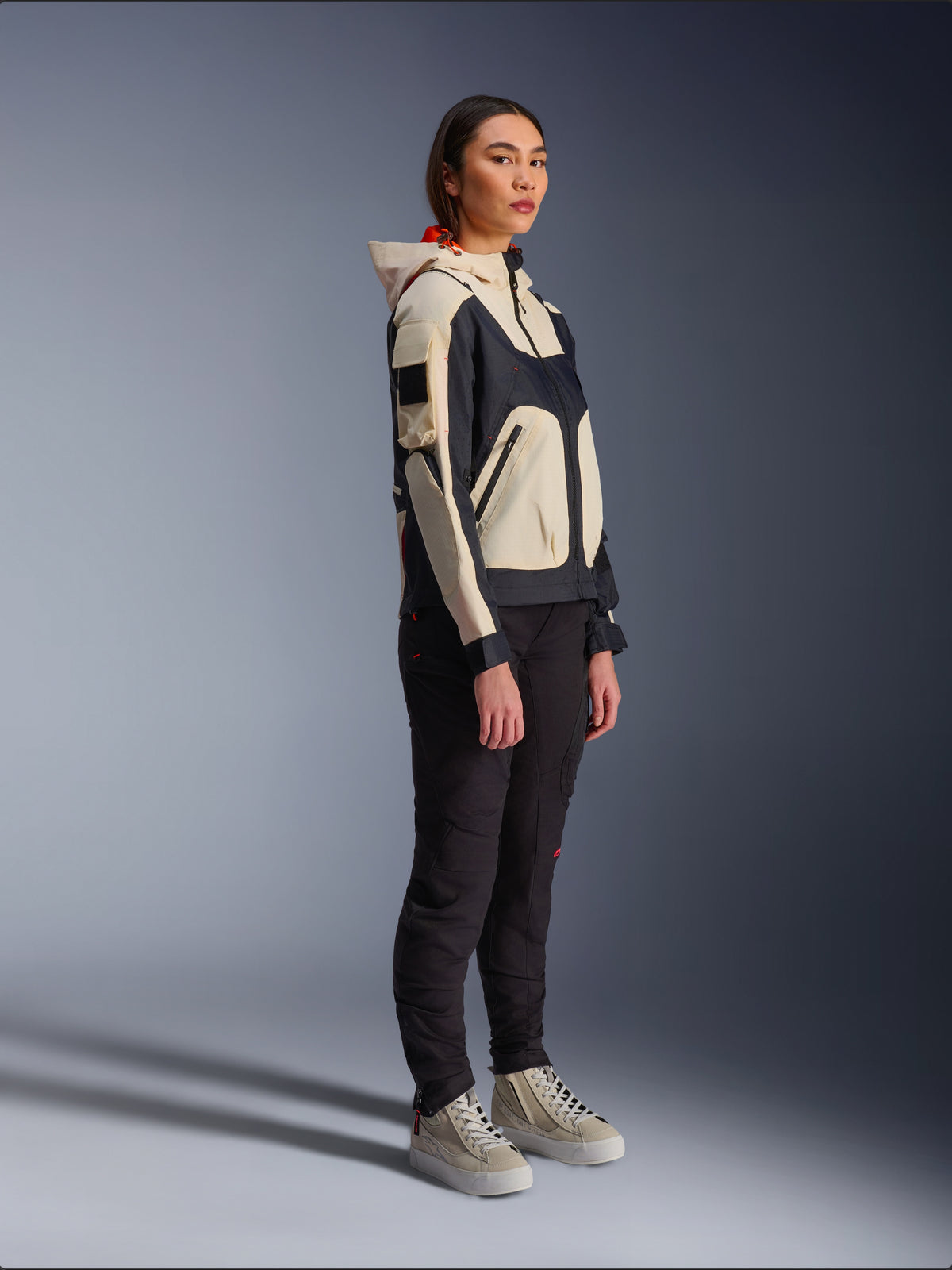 Veste Alpinestars Molly Air en Black Almond, portée par une motarde avec un pantalon noir et des baskets montantes crème, présentant un design bicolore avec des empiècements noirs et beige, une capuche intégrée et un style urbain contemporain.
