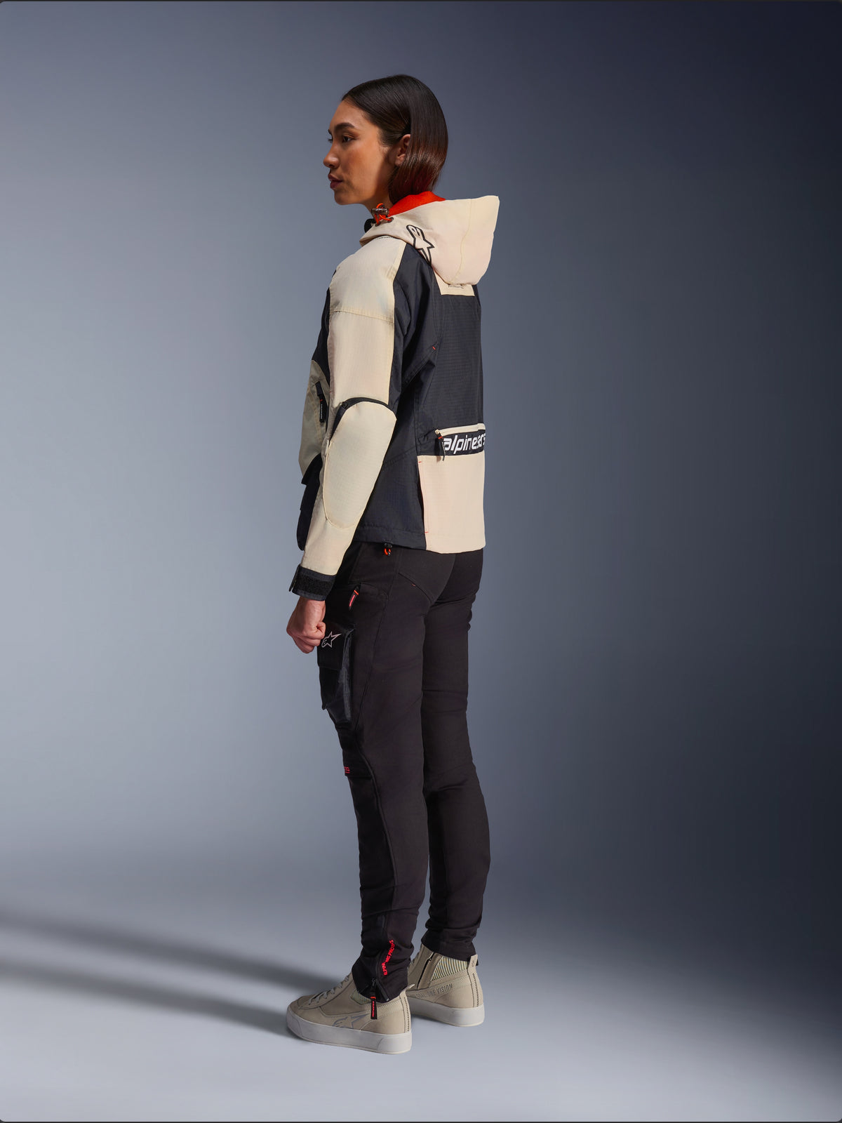Veste Alpinestars Molly Air, veste de moto pour femme, Black Almond, dotée d'un design à capuche avec des manches crème et un buste noir, portée avec un pantalon de moto noir et des baskets beiges, style urbain contemporain.