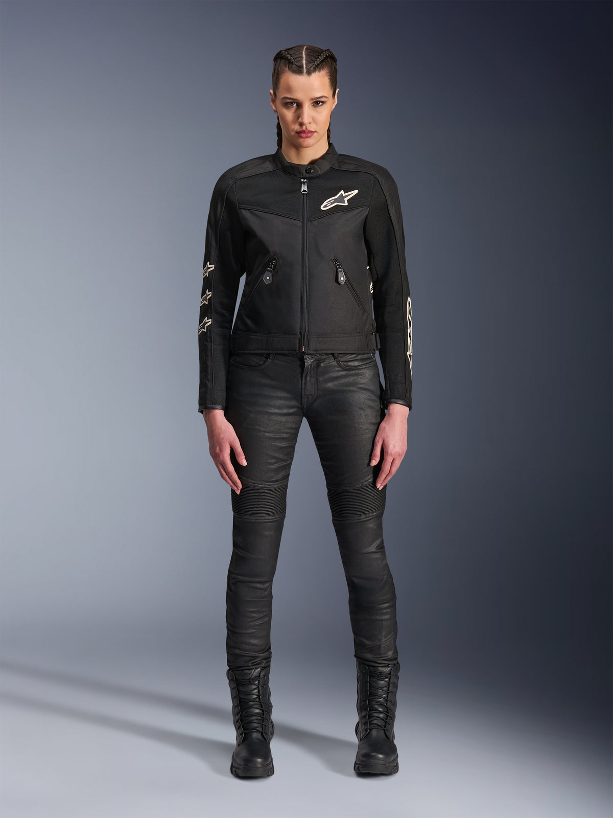 Modèle féminin portant la veste Alpinestars Stella T-Dyno Air, veste de moto noire pour femme avec panneaux en maille 3D et logos Astars blancs, accompagnée d'un pantalon de moto slim noir et de bottes à lacets noires, style d'équipement de conduite urbaine.