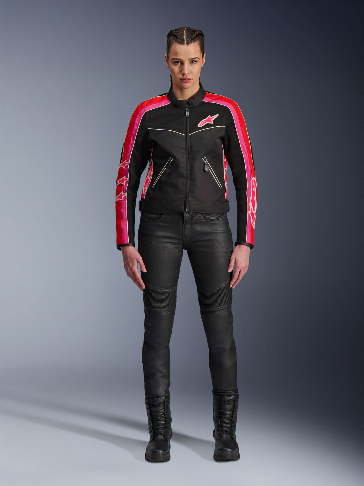 Female rider wearing the Alpinestars Stella T-Dyno Air Jacket, Black with Bright Red and Fuchsia accents, paired with black motorcycle pants and lace-up boots, featuring 3D mesh panels, tailored fit, and pink star logos, urban riding gear outfit