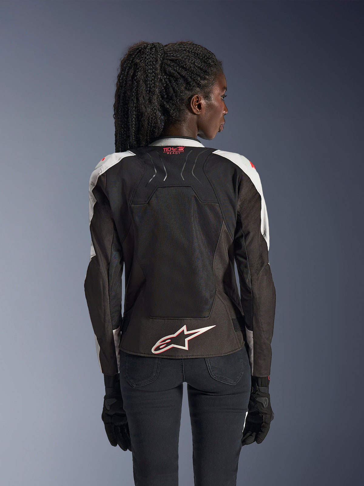 Veste Alpinestars Stella SMX Air, veste de moto pour femme, gris glacé et noir avec accents corail fluo, vue arrière montrant le marquage Tech-Air Ready et le logo Astar blanc, châssis en mesh pour une ventilation élevée, coupe de style sportif