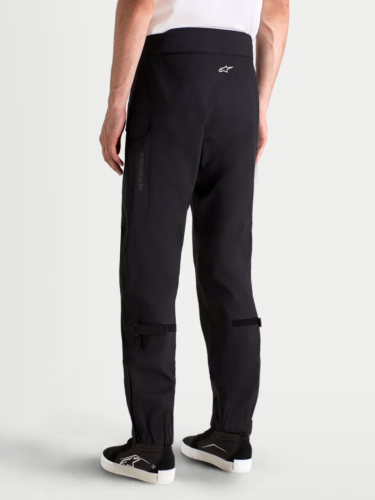Alpinestars Juggernaut V2 Drystar Pantalons, pantalon de moto urban étanche pour homme noir, vue de dos sur un modèle portant des bottes assorties, doté d'une taille haute et de poches cargo