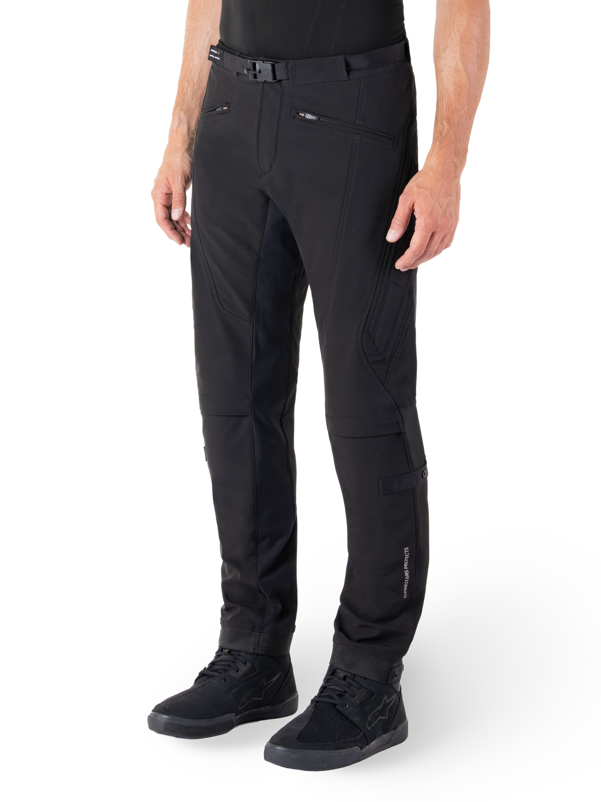 Pantalon Alpinestars Alden, pantalon de moto urbain, noir, tissu softshell technique avec coupe régulière, doté d'une boucle de taille magnétique, d'empiècements latéraux matelassés, de poches zippées et d'un logo discret sur le bas de la jambe, porté avec des chaussures de moto noires
