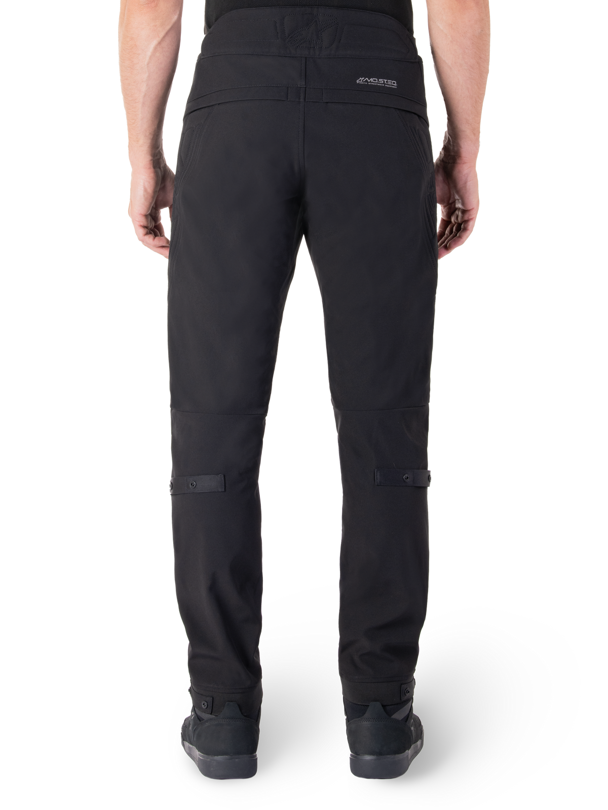 Pantalon Alpinestars Alden, pantalon de moto urbain noir, vue arrière, avec mot-symbole réfléchissant MO.ST.EQ. sur l'empiècement arrière, coupe ajustée sous le genou et boutons-pression de réglage du volume aux mollets et aux chevilles, design textile technique d'inspiration streetwear.