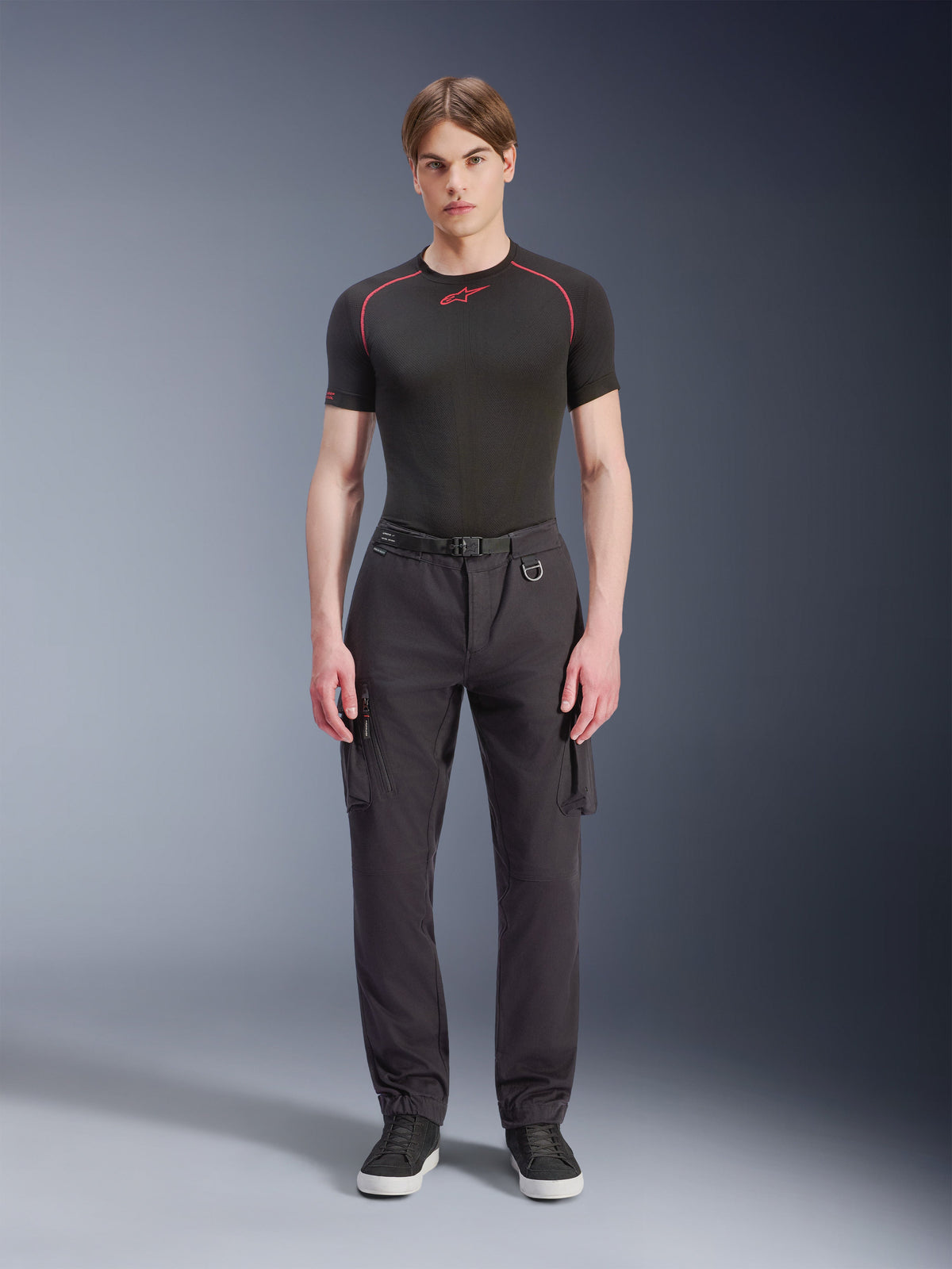 Pantalon Cargo Alpinestars Flex-AST - Court, noir, porté par un mannequin homme avec un t-shirt technique noir et des baskets noires, pantalon de moto urbain doté de multiples poches cargo, d'une coupe fuselée et d'une ceinture intégrée avec boucle et anneau en D