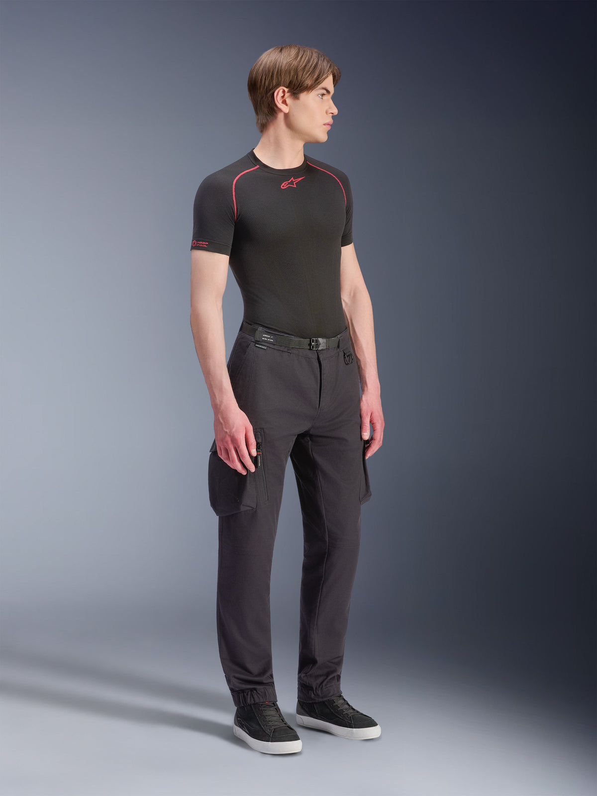 Modèle masculin portant le pantalon cargo Alpinestars Flex-AST - Court en noir, pantalon cargo de moto urbain avec poches latérales et jambes fuselées, associé à une sous-couche technique noire et des baskets, tenue de moto urbaine.