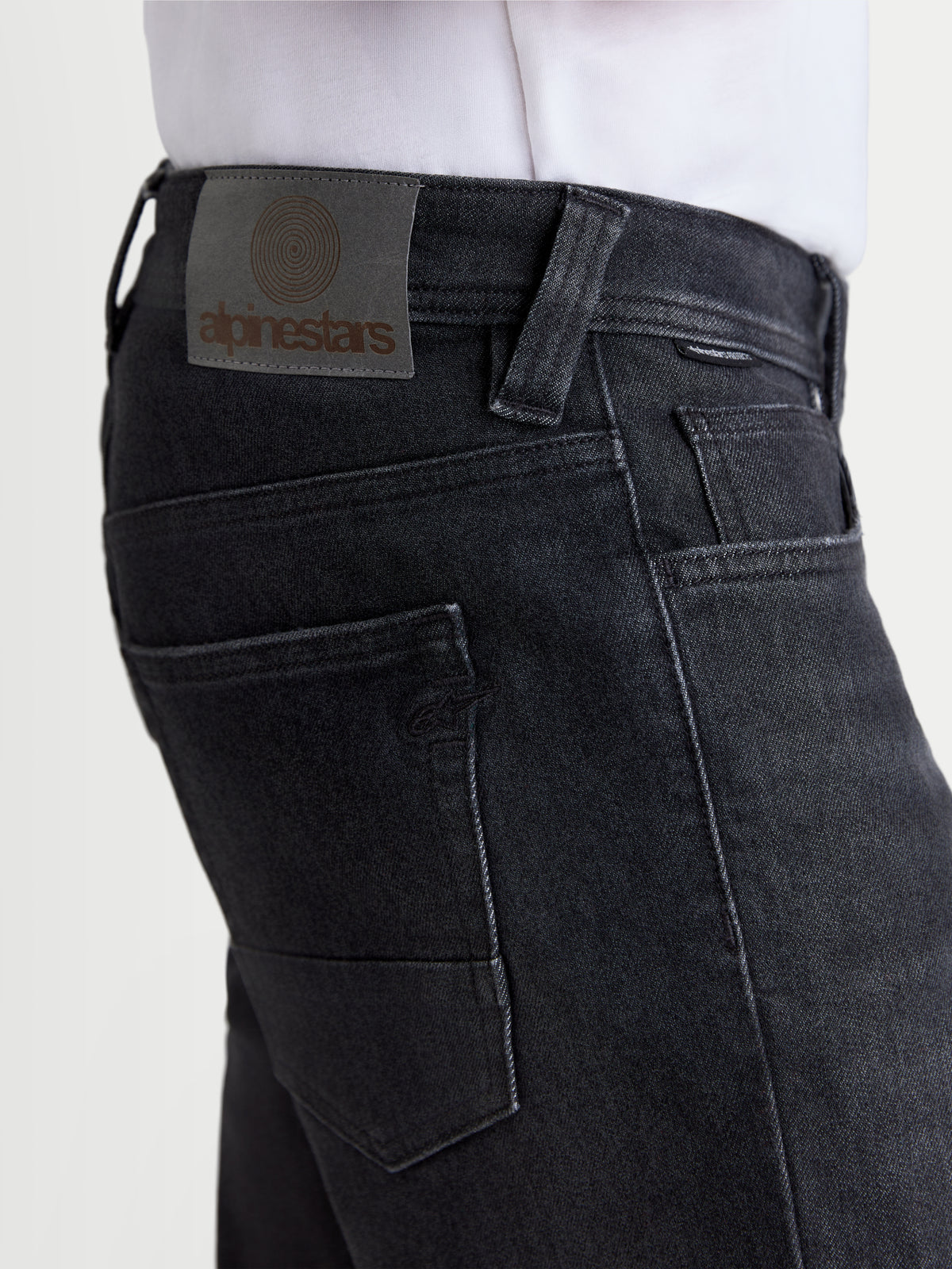 Alpinestars Flex Ast 8 Denim Pantalons, pantalon de moto urbain en denim noir, vue rapprochée mettant en valeur l'écusson en cuir au dos et les poches arrière sur un modèle