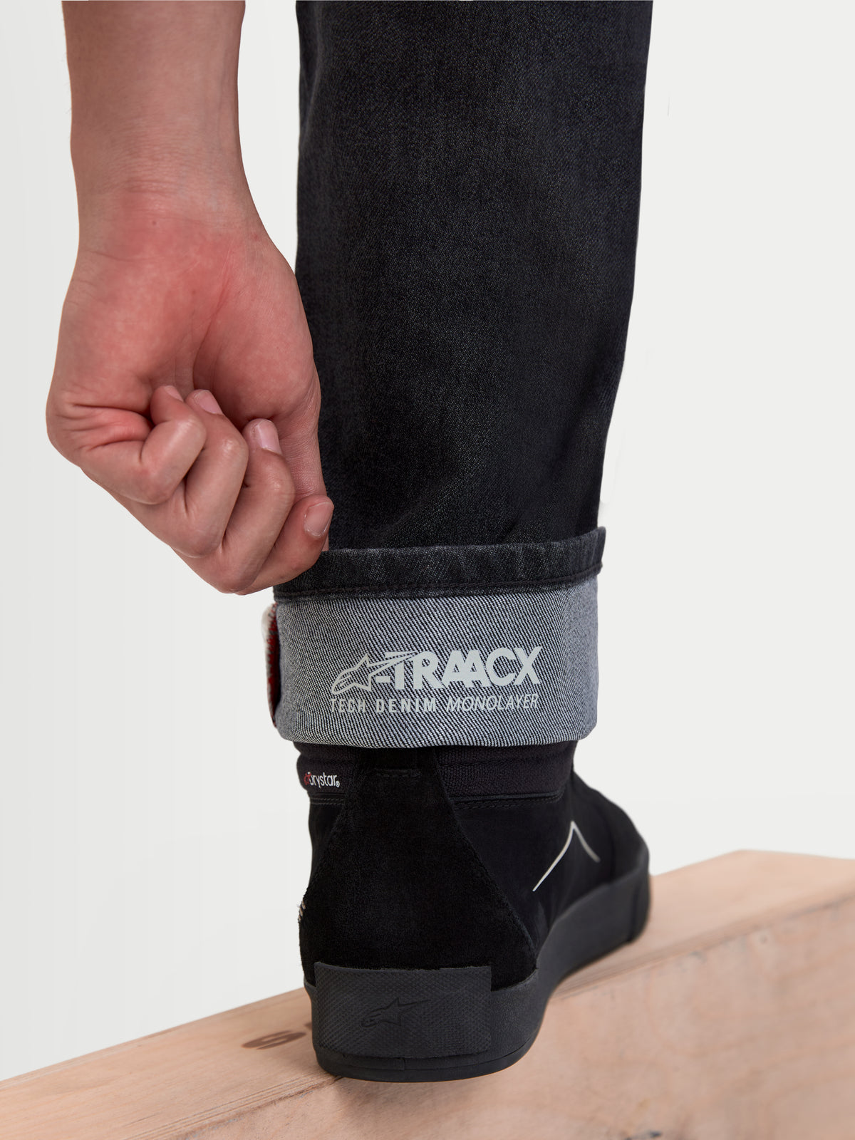 Alpinestars Flex Ast 8 Denim, pantalon de moto urbain en denim noir, vue en gros plan du bas de jambe retroussé mettant en valeur la construction en denim technique monocouche A-TRAACX et le marquage intérieur