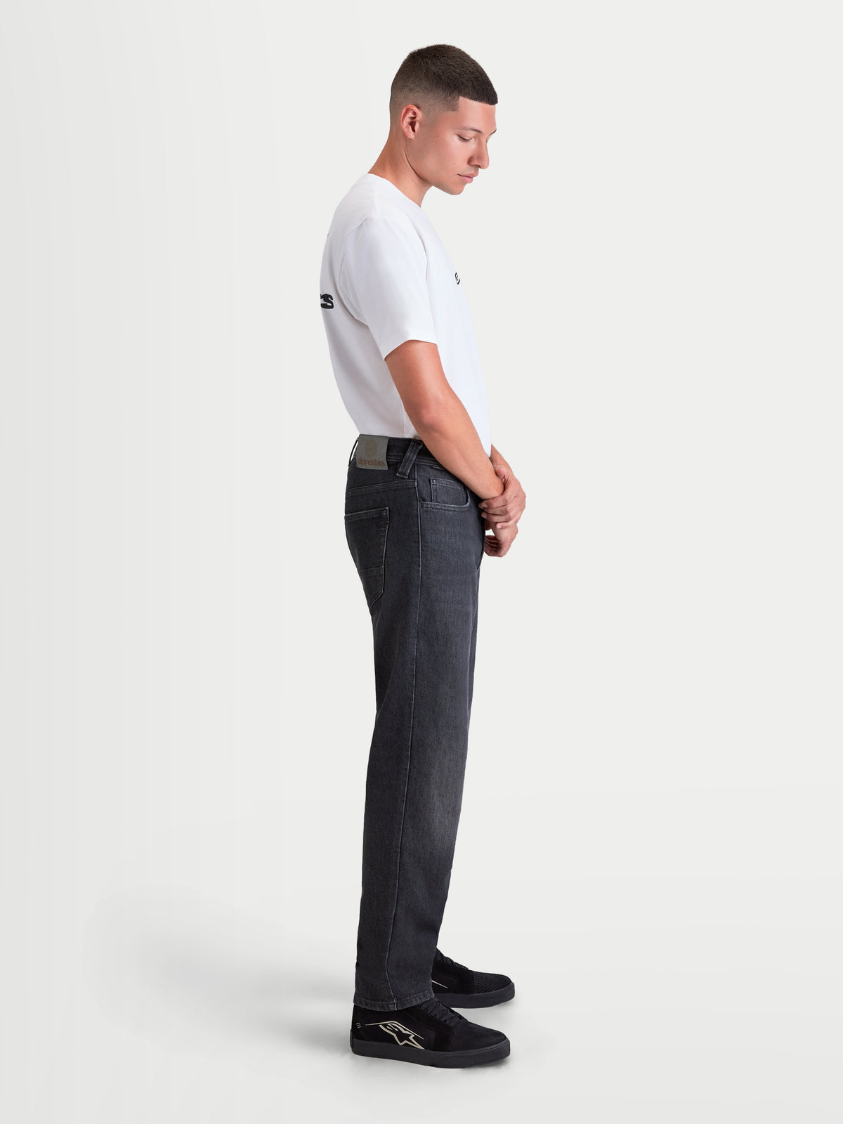 Alpinestars Flex Ast 8 Denim Pantalons, pantalon de moto urbain pour homme en noir délavé, vue de profil sur un modèle portant un t-shirt blanc et des chaussures de moto casual, denim monocouche de protection