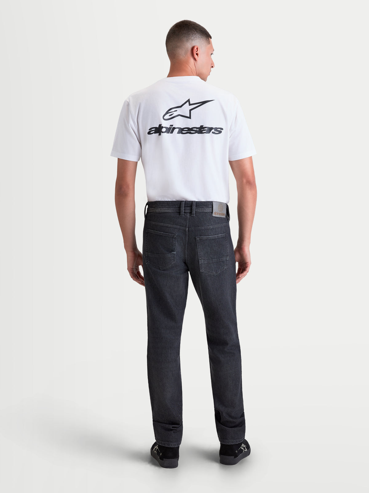 Alpinestars Flex Ast 8 Denim Pantalons, pantalon de moto urbain contemporain pour homme en noir délavé, vue de dos sur un modèle portant le denim monocouche homologué AA avec un patch en cuir à l'arrière et des poches arrière brodées