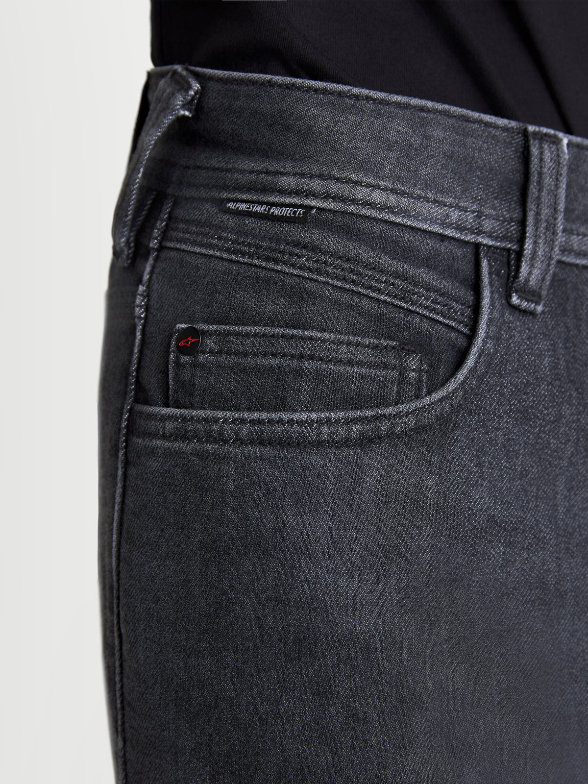 Alpinestars Flex-AST 7 Denim Pantalons, pantalon de moto urbain en denim noir délavé, vue rapprochée montrant la construction des poches, les rivets griffés et l'étiquette tissée Alpinestars Protects