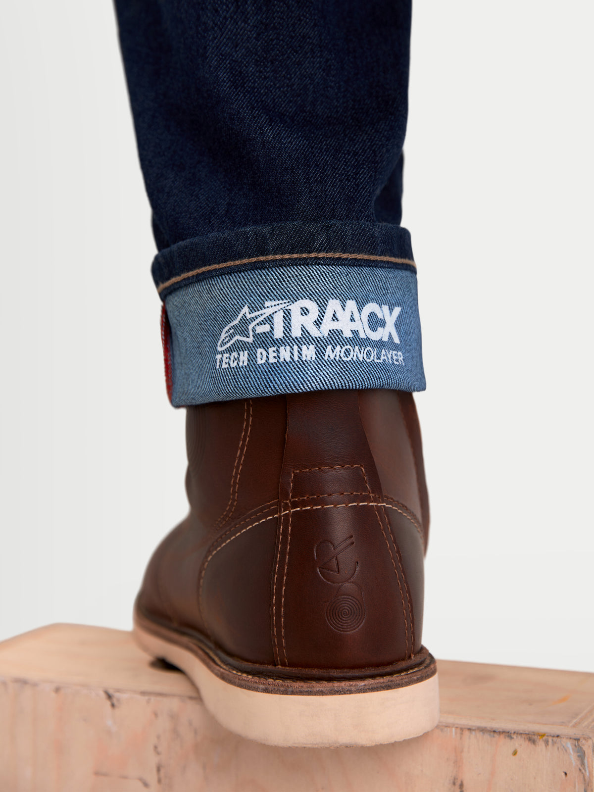Alpinestars Flex-AST 7 Denim Pantalons, jean de moto urbain pour homme, bleu foncé, vue rapprochée de l'ourlet à revers montrant le marquage de denim technique A-TRAACX et des bottes en cuir marron