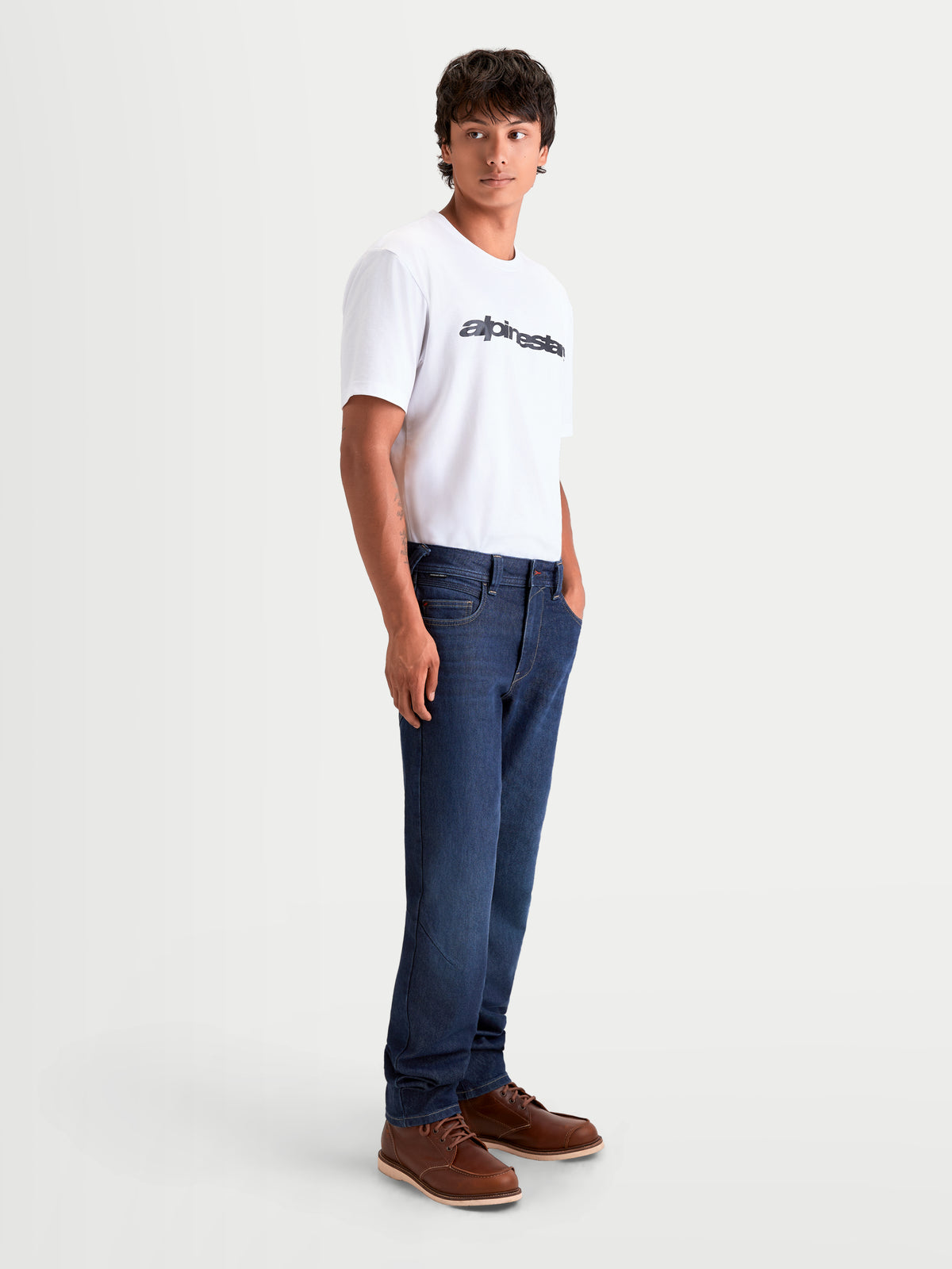 Alpinestars Flex Ast 7 Denim Pantalons, pantalon de moto urbain contemporain pour homme bleu foncé, vue de profil latéral porté par un modèle avec un t-shirt blanc et des bottes marron