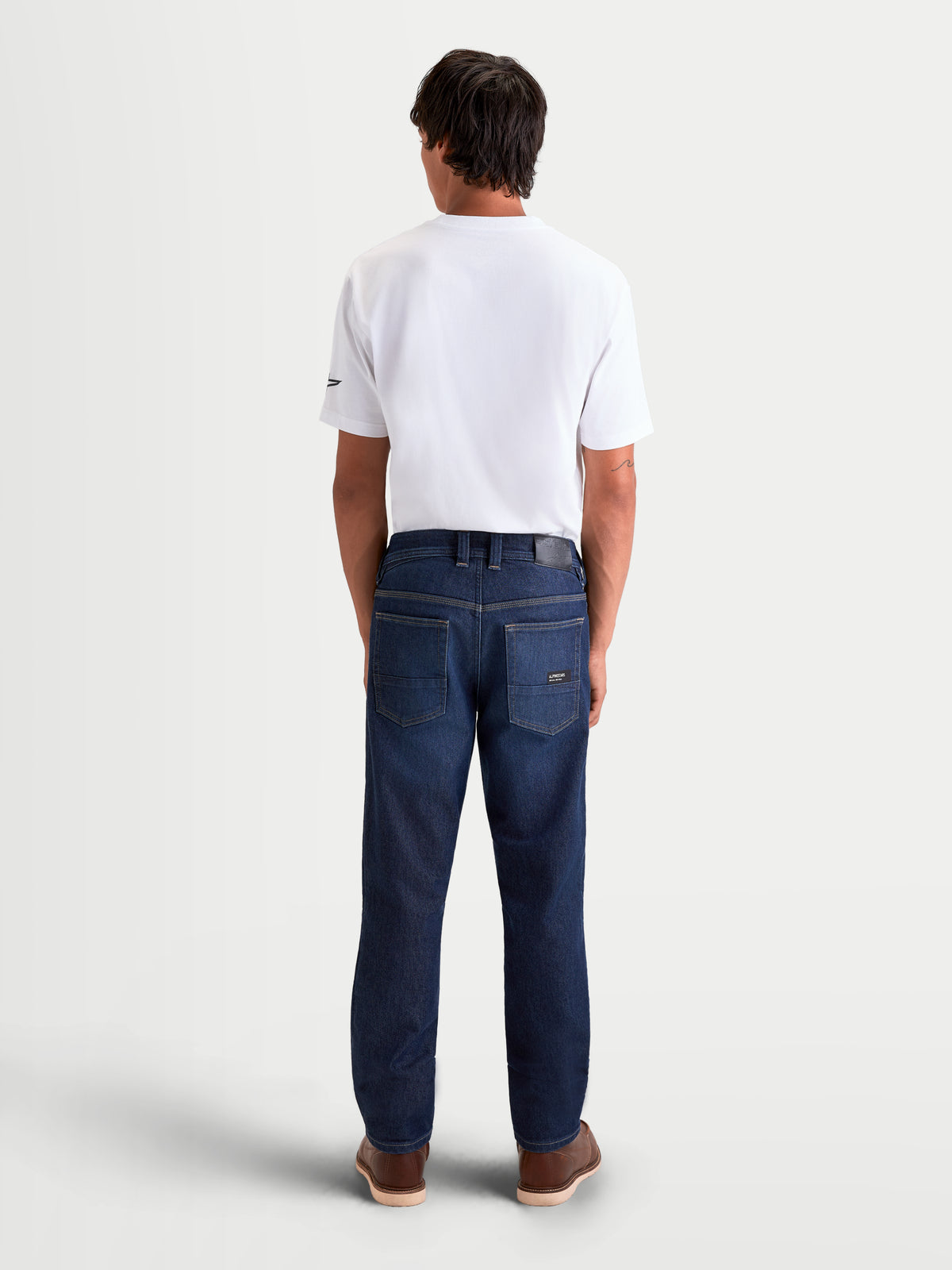 Alpinestars Flex-AST 7 Denim Pantalons, pantalon de moto urbain pour homme en denim bleu foncé, vue de dos montrant la construction monocouche, le patch en cuir à l'arrière et les détails de la poche brodés portés sur un modèle