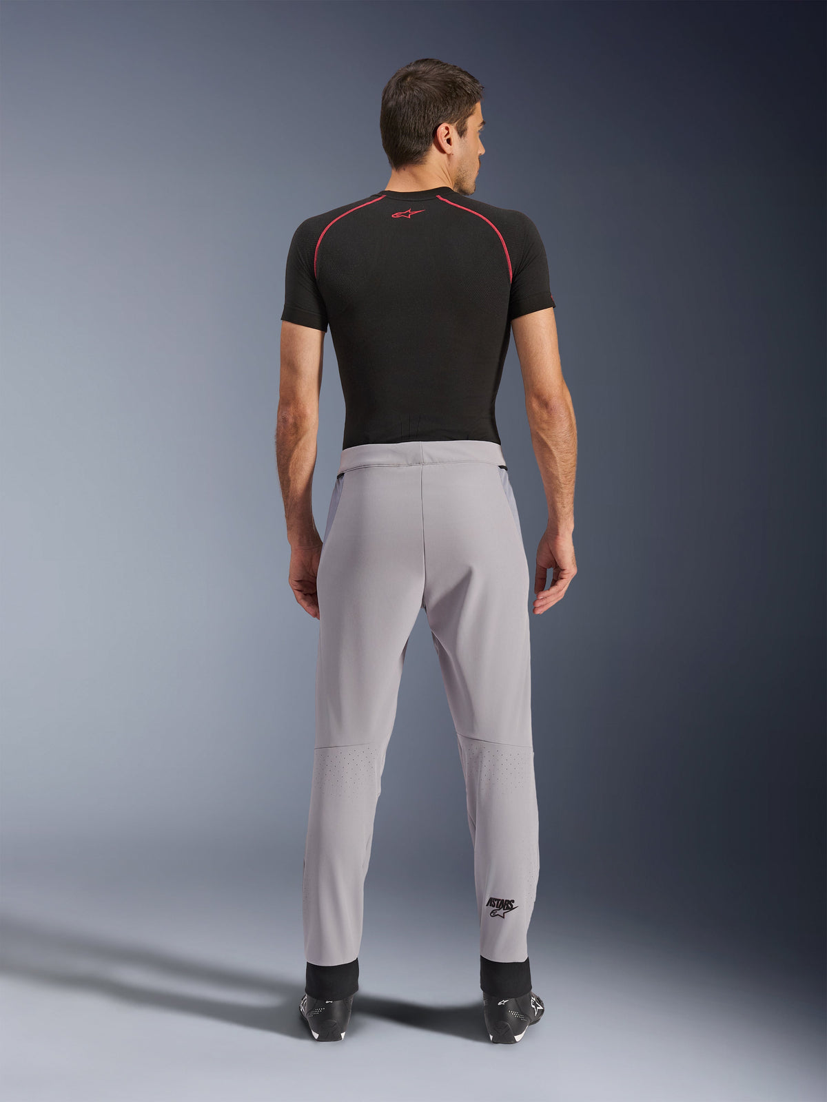 Alpinestars Aeroshell Airflow Pants, Mid Gray, back view showing laser-perforated zones on the calves, lightweight stretch softshell construction, worn with a black short-sleeve shirt and motorcycle boots, sport-fit design for warm weather riding