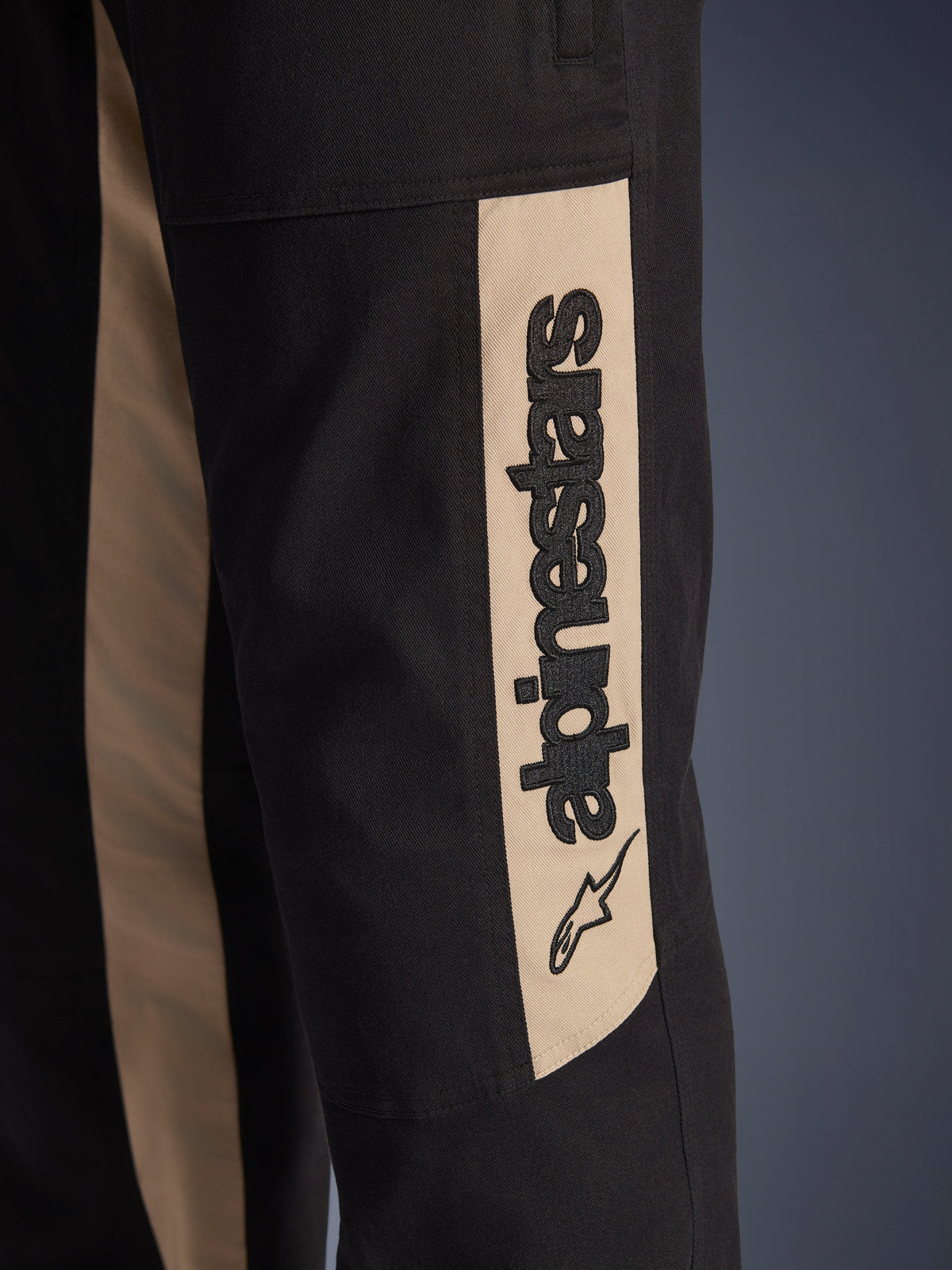 Pantalon Alpinestars Flex-AST Canvas, gros plan sur le côté de la jambe, noir avec panneau d'accentuation couleur aluminium, arborant un logo Alpinestars vertical noir et une icône d'étoile, sergé de polycoton résistant pour la conduite moto urbaine