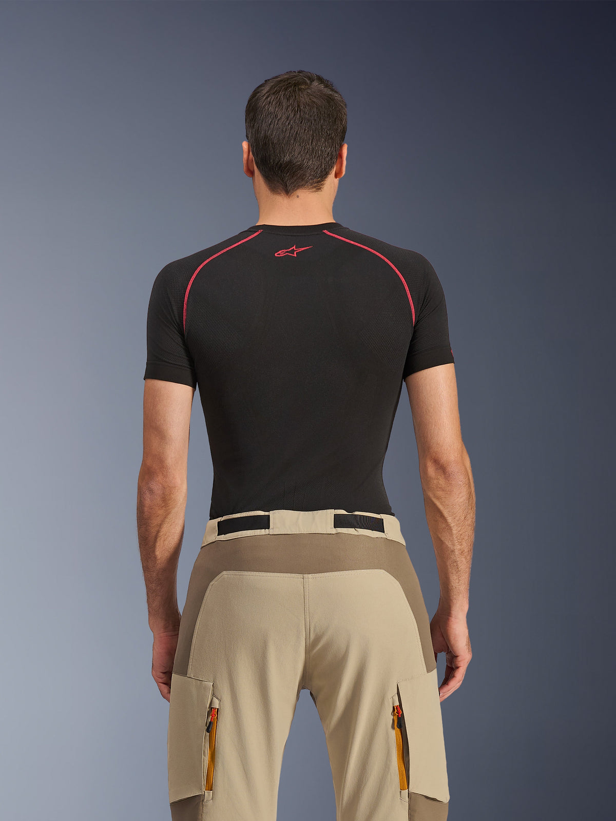 Alpinestars Maxdura Dual Pants, Adventure Motorcycle Pants, Walnut Aluminum, rear view showing reinforced seat panel and beige stretch fabric, zippered cargo pockets with orange pulls, worn with a black Alpinestars base layer shirt.