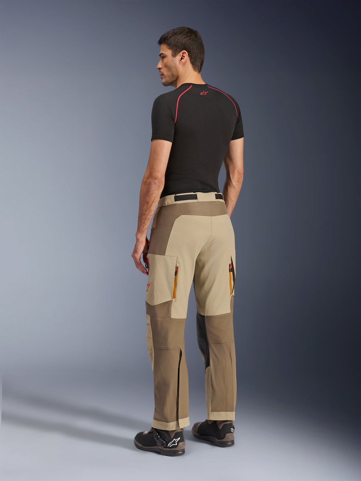 Alpinestars Maxdura Dual Pants, Adventure and Dual-Sport Riding Pants, Walnut Aluminum, rear view worn by a model with a black base layer and riding boots, featuring multi-panel construction with zippered rear vents and reinforced overlays.