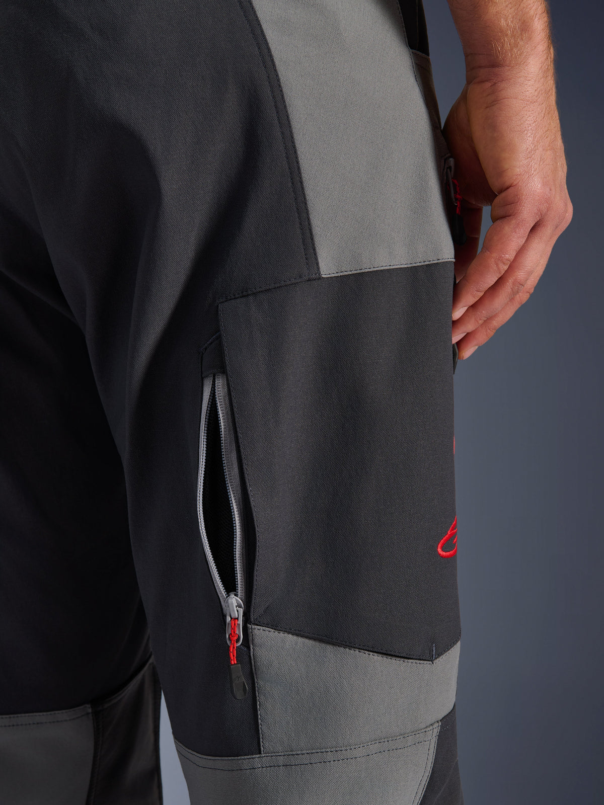 Alpinestars Maxdura Dual Pants, pantalon de moto d'aventure gris foncé et gris anthracite, gros plan sur la cuisse avec une aération zippée et un logo brodé rouge, construction durable en polyamide extensible.