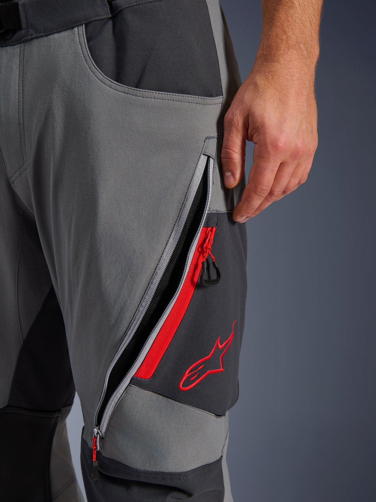 Pantalon Alpinestars Maxdura Dual, pantalon de moto d'aventure gris foncé, vue rapprochée d'une aération zippée sur la cuisse avec détails rouges et logo étoile brodé, conception technique en tissu extensible