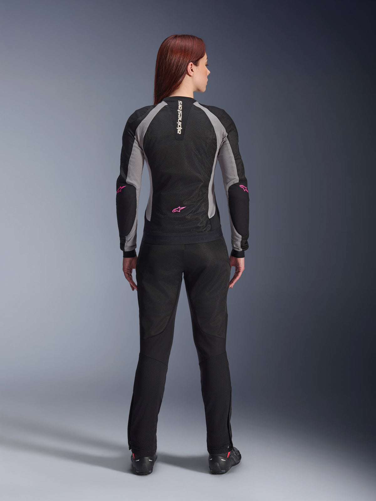 Veste Stella Troop-Air Femme et pantalon assorti Alpinestars vus de dos, Noir Gris Cendré et Rose Fluo, équipement de moto en maille légère avec panneaux gris et touches de rose fluo, marquage Alpinestars vertical et logos étoiles.
