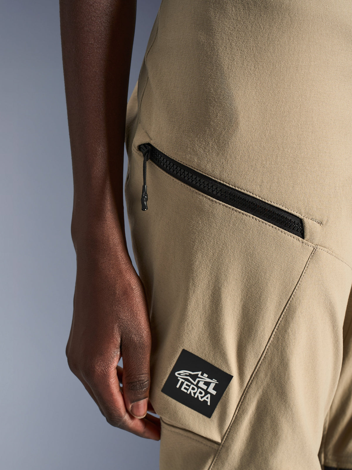 Pantalon Alpinestars Stella Flex-AST Explorer, pantalon de moto pour femme, sable, gros plan sur la poche cargo zippée et le patch logo noir ALL TERRA, construction textile ripstop durable pour l'aventure touring
