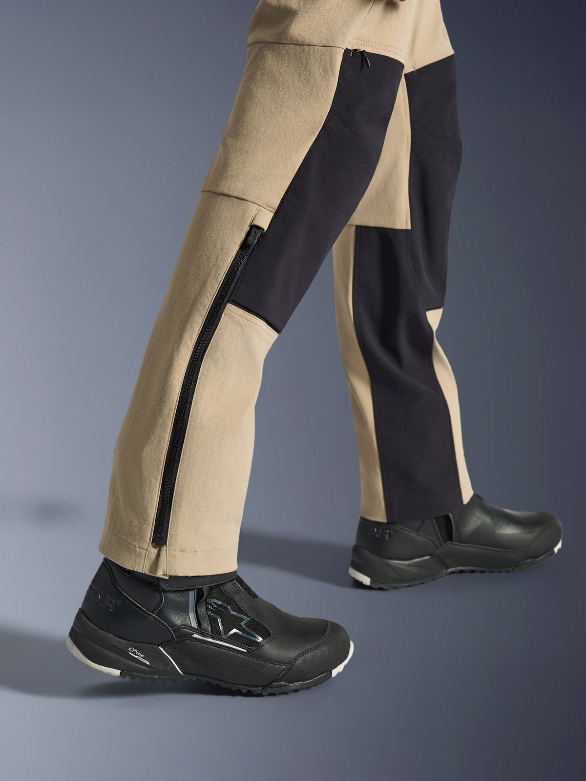Alpinestars Stella Flex-AST Explorer pour femme, pantalon d'aventure moto, sable et noir, vue rapprochée du bas des jambes et des chevilles avec une longue fermeture éclair latérale et des panneaux de renfort noirs, porté avec des chaussures de moto Alpinestars noires.