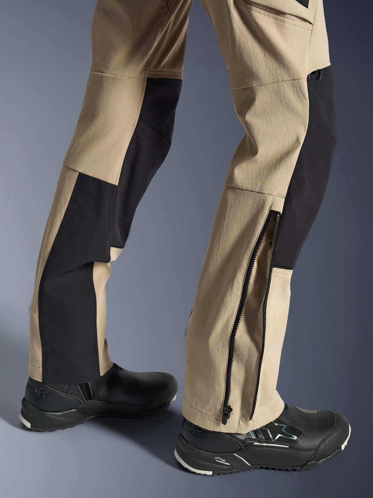 Pantalon Alpinestars Stella Flex-AST Explorer, pantalon de moto pour femme, sable et noir, gros plan sur le bas des jambes montrant un ourlet zippé pour l'ajustement des bottes, porté avec des chaussures de moto Alpinestars noires, doté de panneaux en ripstop durable et en textile extensible respirant.