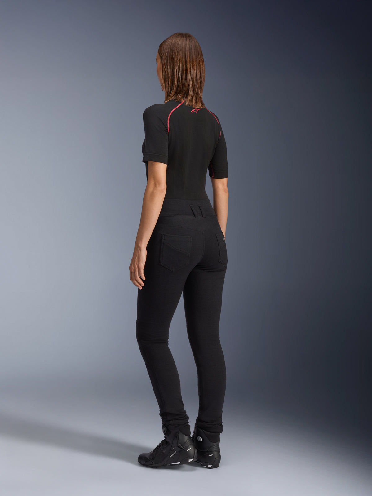 Alpinestars Womens Banshee Leggings, Black, rear view showing figure-hugging anatomical stretch fit and back pockets, worn with a black short-sleeved top and motorcycle boots, sleek urban motorcycle gear for women