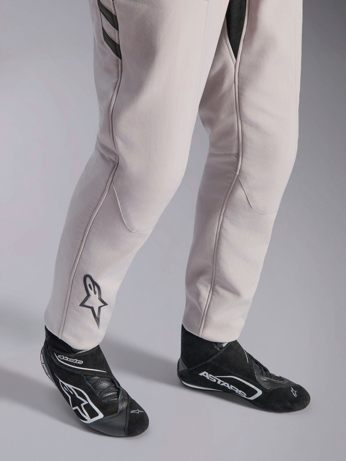 Alpinestars GP Race V3 Suit FIA, combinaison de course automobile Silver Anthracite, vue détaillée du bas des jambes et des bottines de course noires, avec le logo Astars noir sur le mollet, équipement de sport automobile professionnel avec bords-côtes.