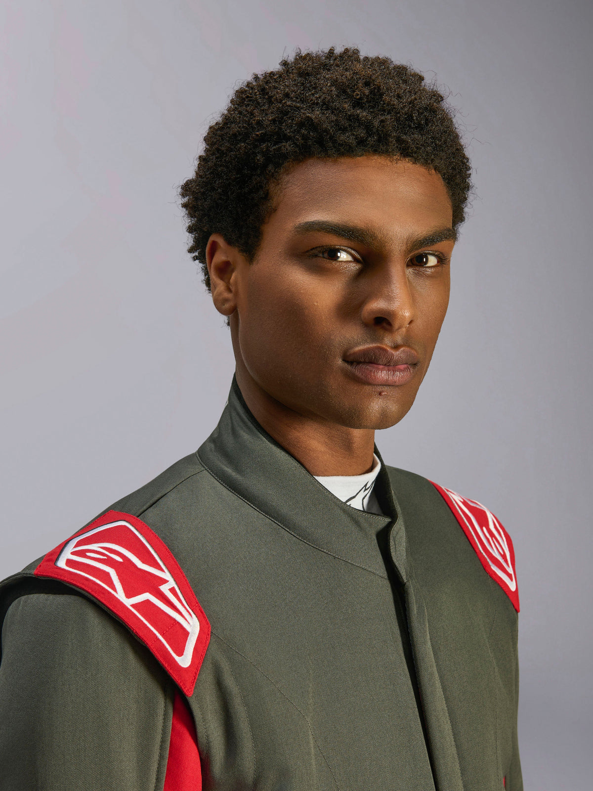 Alpinestars GP Race V3 Suit FIA, Auto Racing Suit, Anthracite Red, close-up of the upper torso and head, featuring red shoulder epaulettes with white Alpinestars logo, high collar and grey twill material