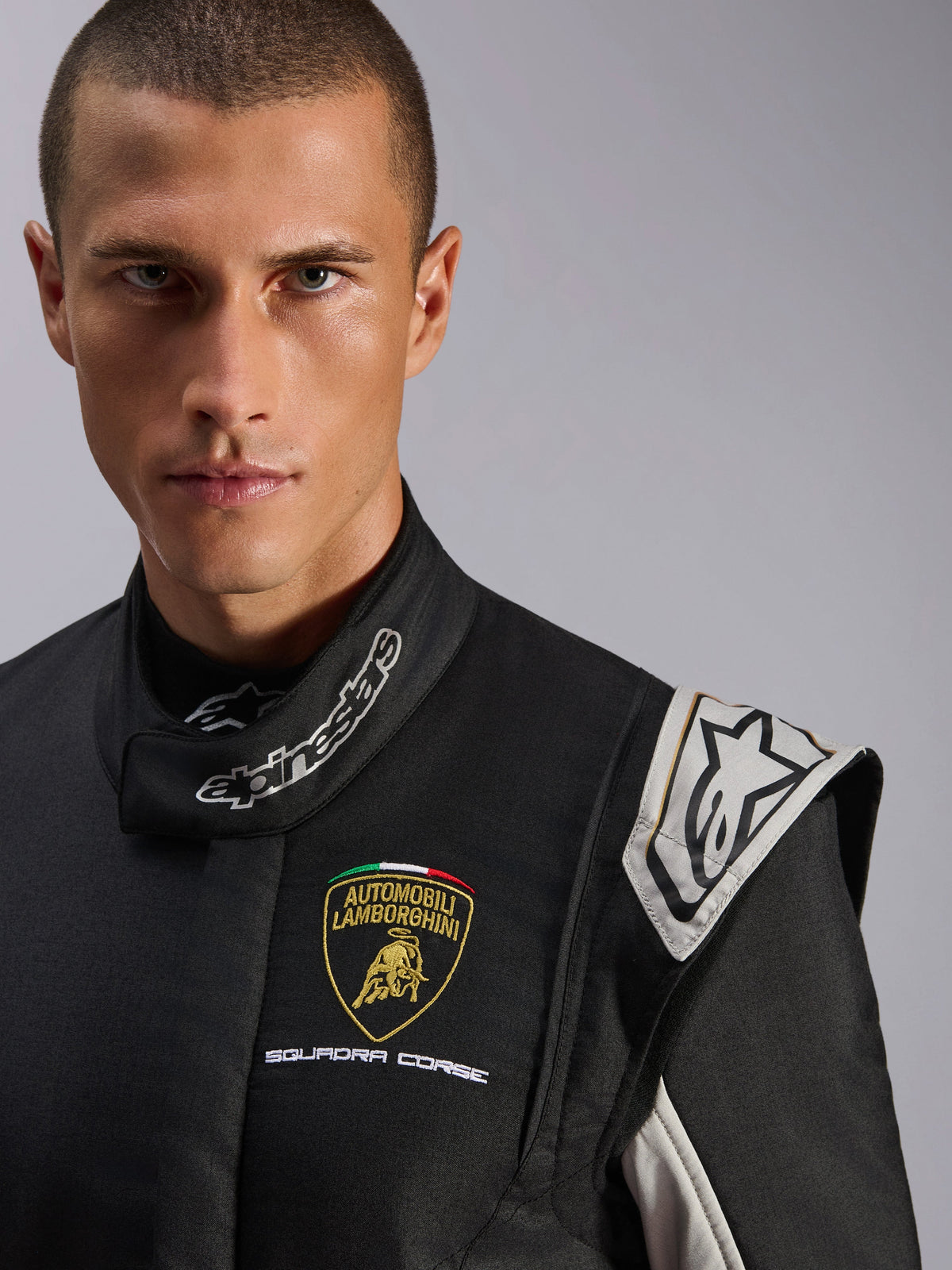 Alpinestars Limited Edition Lamborghini GP Tech V4 Suit, professional racing suit, Black with Silver and Gold accents, close-up featuring Lamborghini Squadra Corse chest logo and Alpinestars neck branding, premium motorsport protection