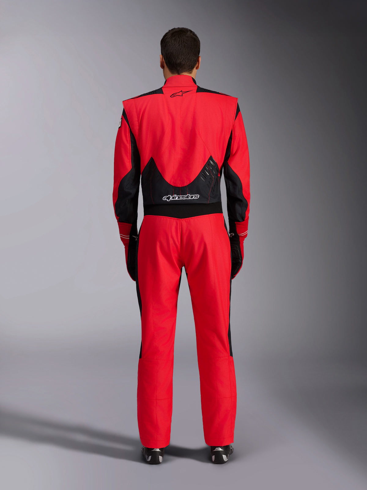 Combinaison de course FIA Alpinestars GP Pro Comp V2, rouge et noir, vue arrière montrant les panneaux en maille noire et extensibles sur le bas du dos, marquage Alpinestars sur le haut et le bas du dos, équipement de course automobile professionnel