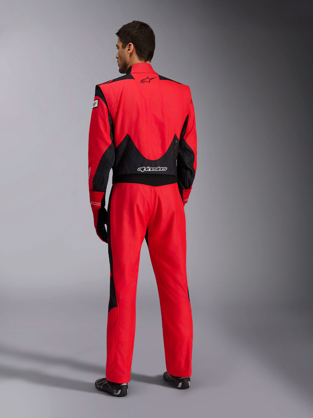 Vue arrière complète de la combinaison de course Alpinestars GP Pro Comp V2 FIA, rouge et noir, avec panneaux en mesh noir respirant sur les épaules et le bas du dos, logo Alpinestars blanc, portée avec gants et bottes de course assortis, équipement professionnel de pilote de sport automobile