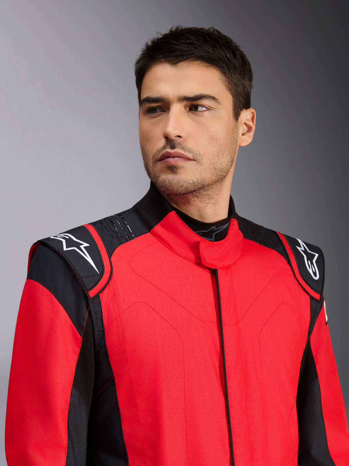 Mannequin homme portant la combinaison de course automobile Alpinestars GP Pro Comp V2 FIA, rouge et noire, avec logos Astars blancs sur les épaules et détails de technologie de grip en silicone, vêtement professionnel de sport automobile