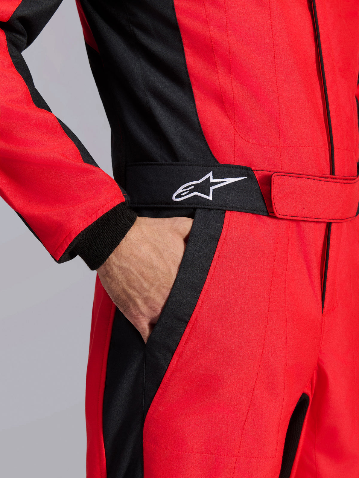 Combinaison de course Alpinestars GP Pro Comp V2 FIA, rouge et noir, gros plan sur la taille montrant une main dans la poche, ceinture noire avec logo étoile blanc, panneaux structurés pour la course automobile