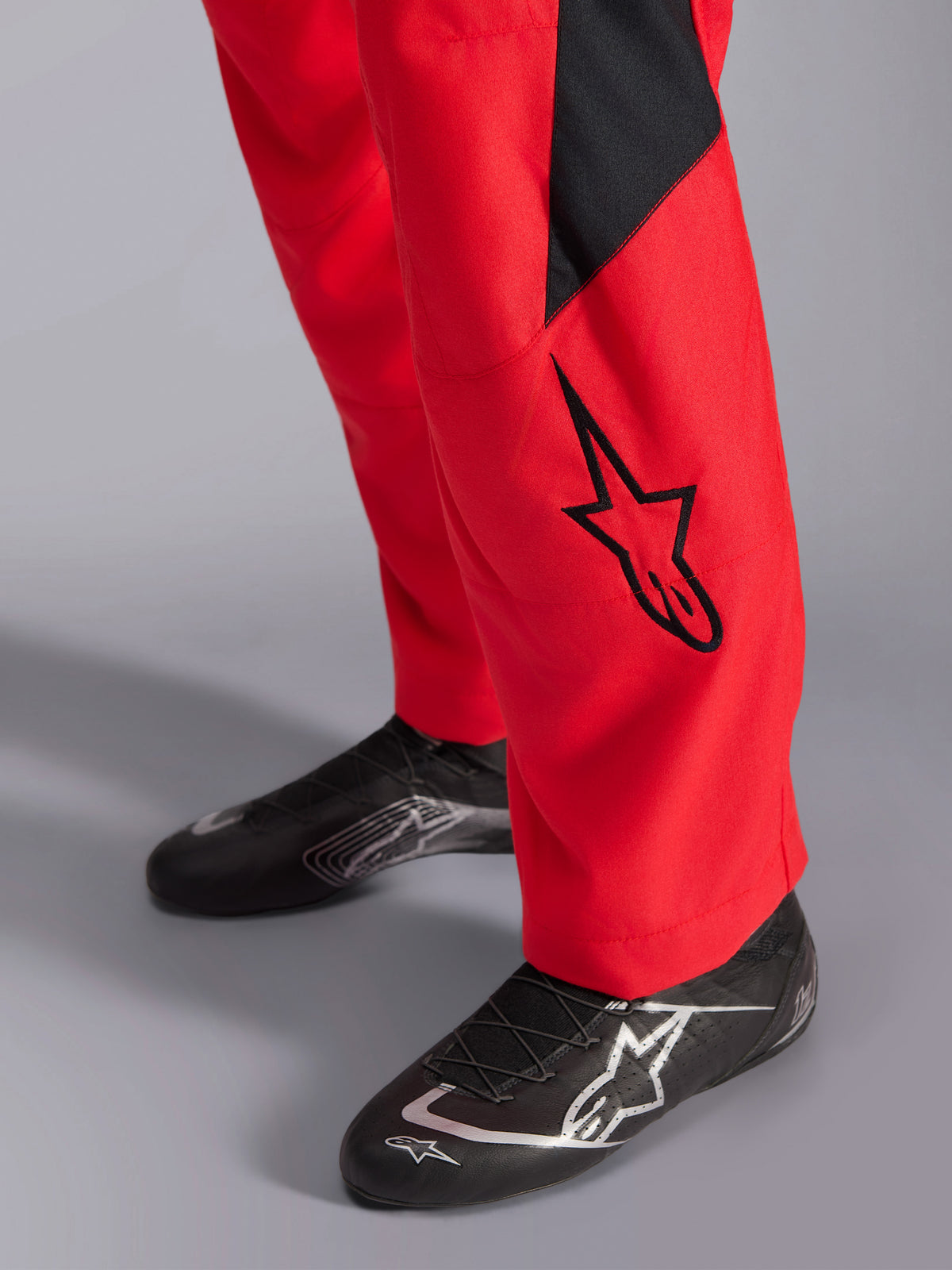Alpinestars GP Pro Comp V2 FIA Racing Suit, gros plan sur le bas de la jambe et les chaussures de course, rouge avec un logo Astars noir et un empiècement noir, associé à des chaussures de course de performance noires, équipement de course automobile.