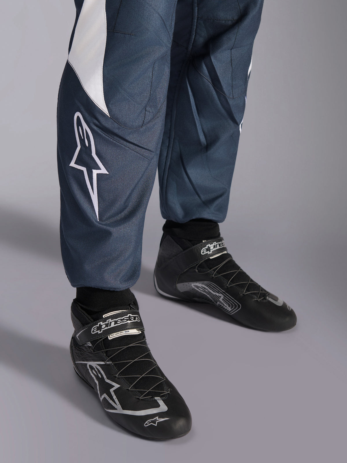 Alpinestars GP Pro Comp V2, combinaison de course FIA bleu cyan et grise, logo étoile et chaussures de course noires.