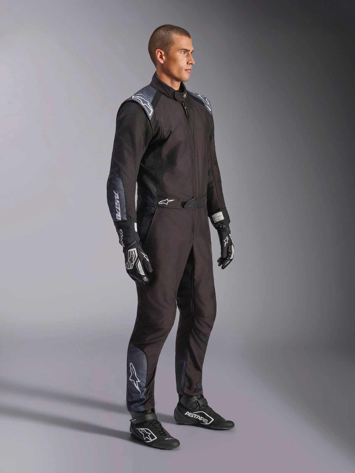 Alpinestars KMX-5 V3 Suit, Karting Suit in Black Dark Shadow, worn with matching black racing gloves and shoes, featuring laser-cut perforations and tech mesh panels, sleek dual-layer design with white branding for professional motorsport