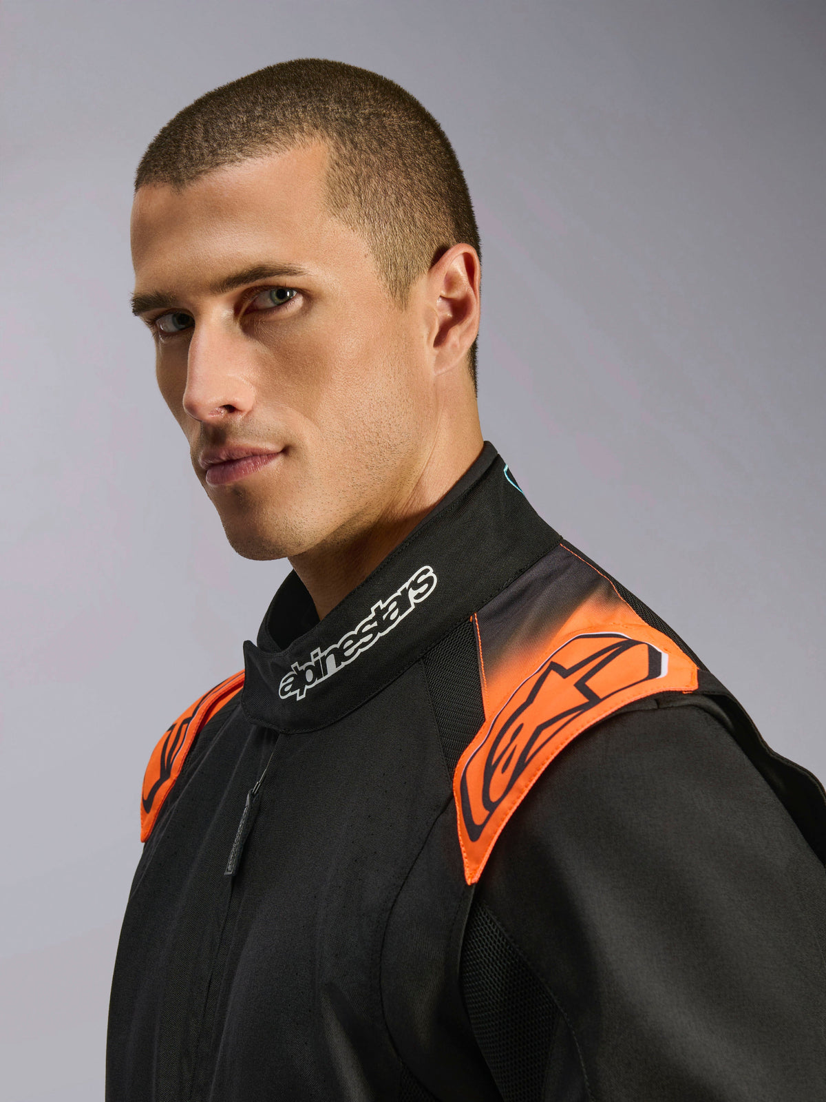 Alpinestars KMX-5 V3, combinaison de karting noire et orange fluo, certifiée FIA, détail du col et des épaules sur mannequin