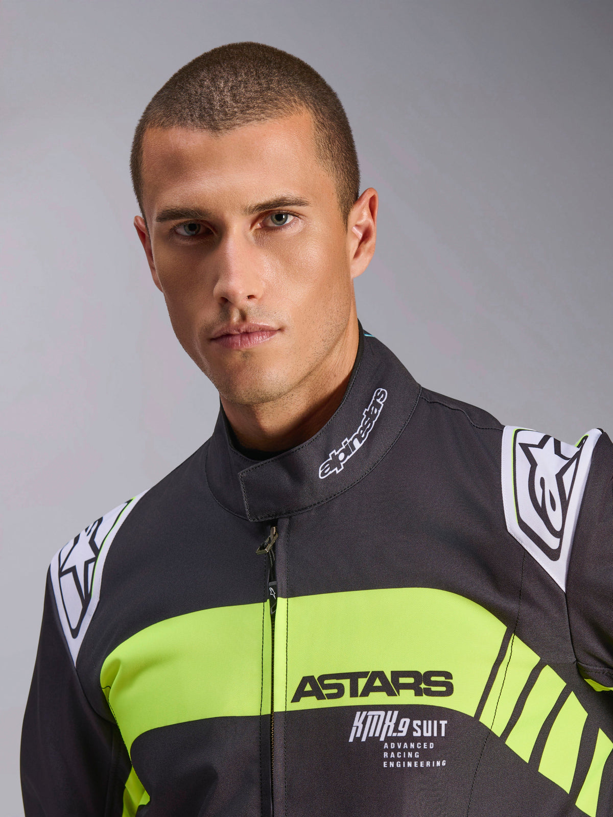 Combinaison Alpinestars KMX-9 V3 Graphic 3, combinaison de karting, noir et jaune fluo, portrait en gros-plan présentant une bande jaune fluo sur la poitrine avec les marquages ASTARS et KMX.9 SUIT, logos Alpinestars sur les épaules et le col, équipement de course professionnel