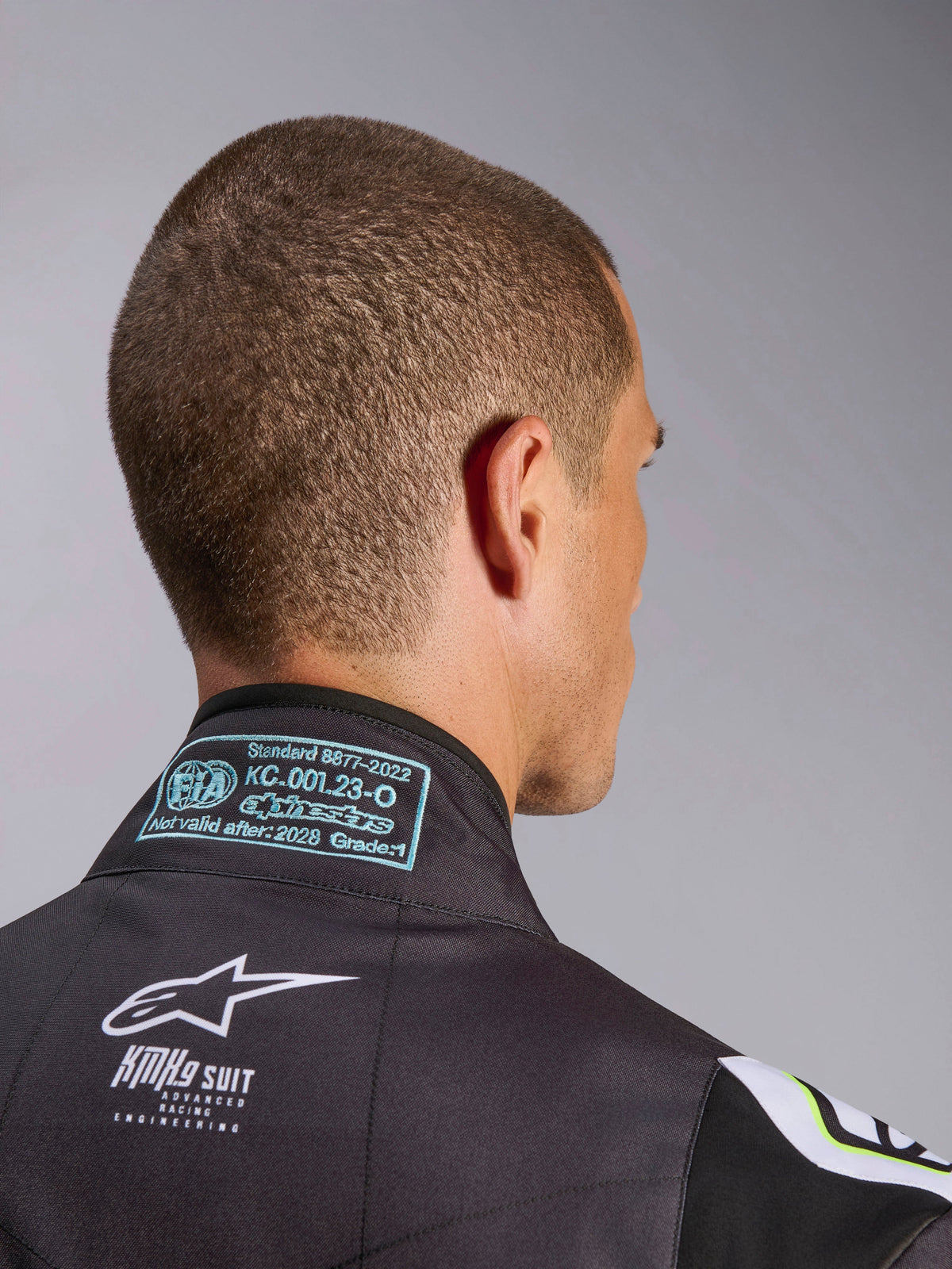 Combinaison Alpinestars KMX-9 V3 Graphic 3, gros plan sur la zone du col arrière, montrant l'étiquette d'homologation FIA 8877-2022 Grade 1 et le marquage KMX-9 blanc sur matériau noir, détail d'équipement de karting