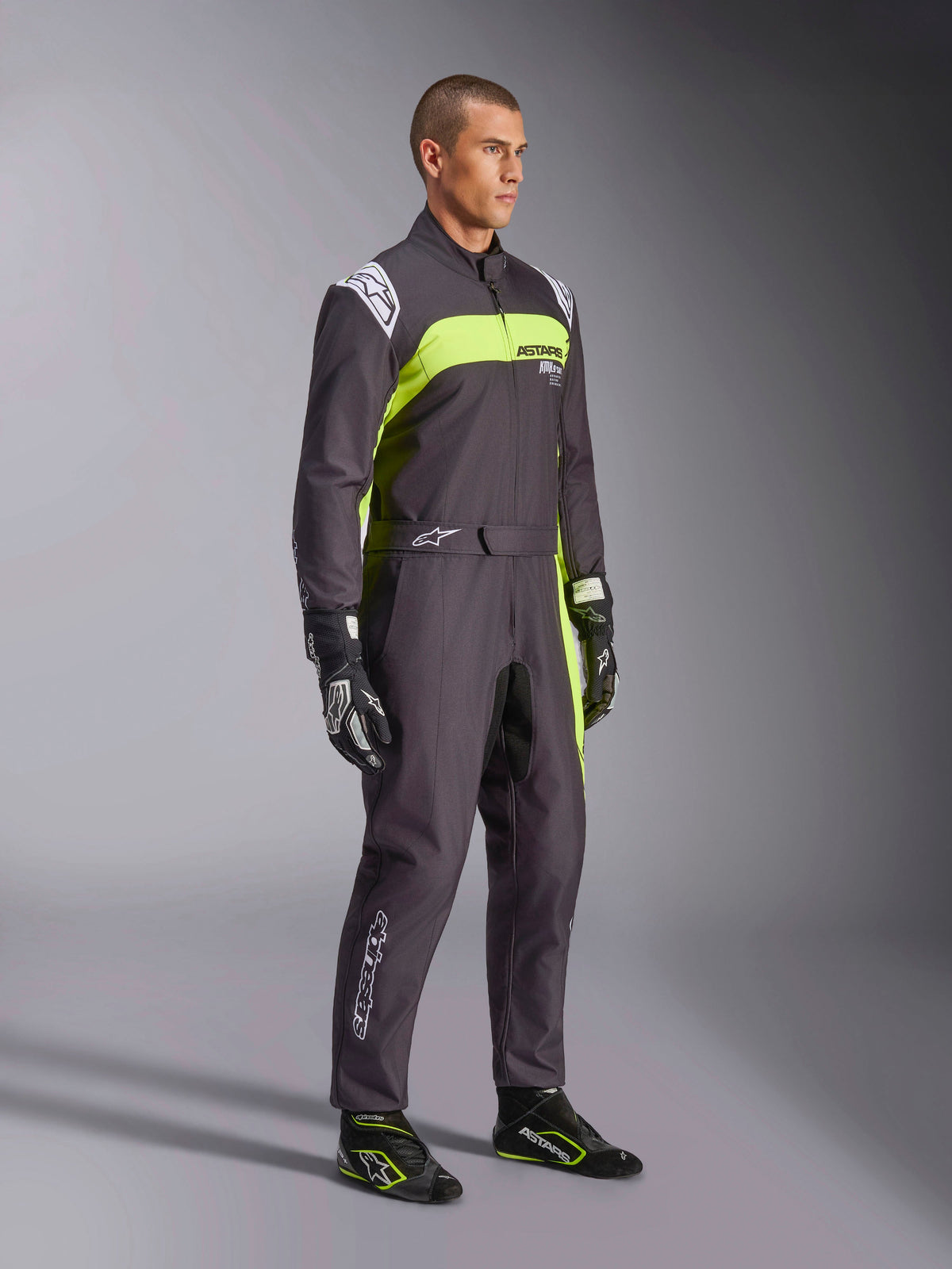 Mannequin homme portant la combinaison Alpinestars KMX-9 V3 Graphic 3 en noir et jaune fluo, équipement de karting professionnel avec panneaux jaune néon éclatants et accents de logo blancs, accessoirisé avec des gants et des chaussures de course coordonnés, sur fond de studio.